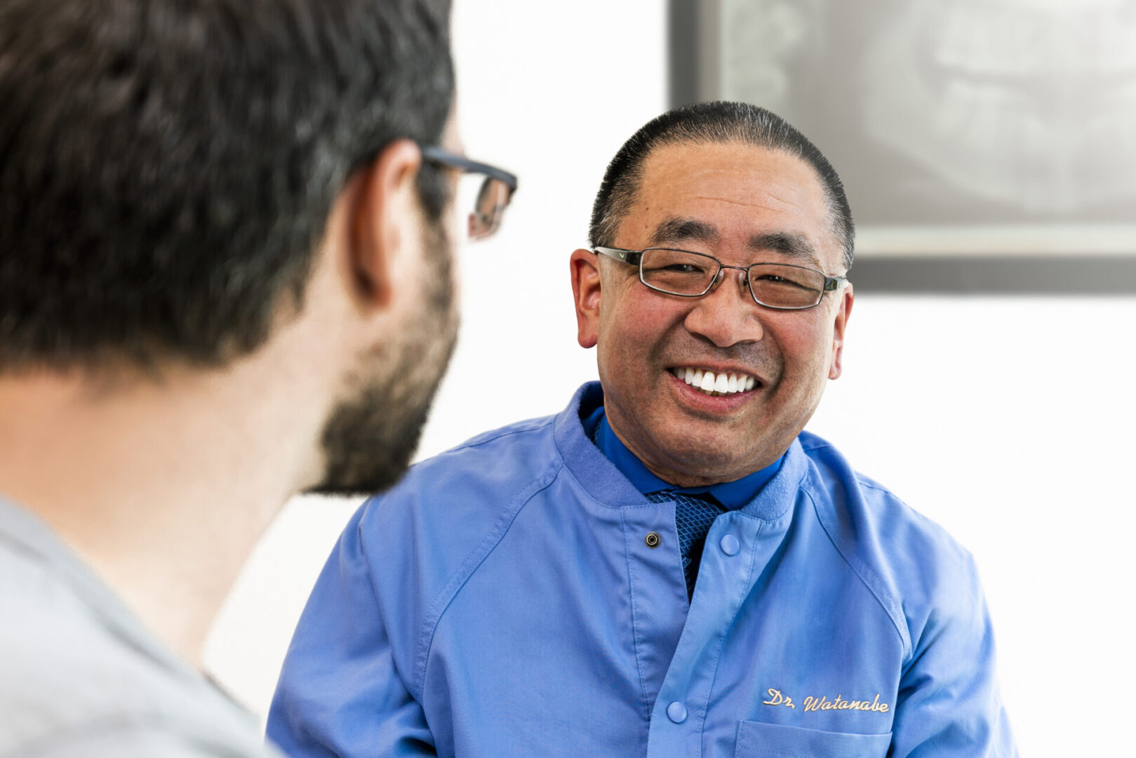 A man in blue shirt smiling at another person.